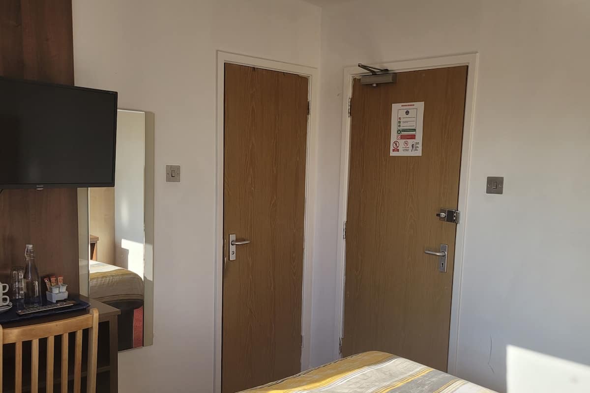 A bedroom with a bed, a TV mounted on the wall, and two doors.