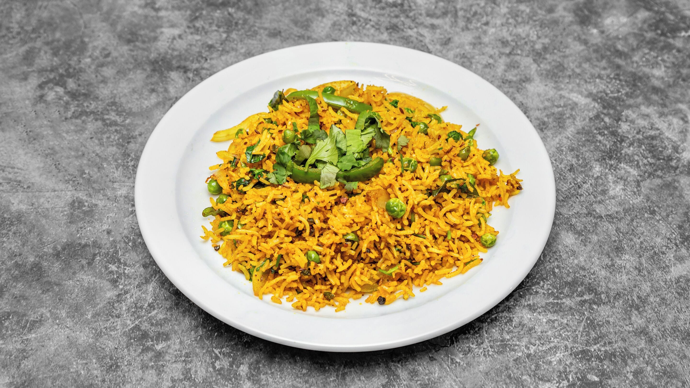 A plate of yellow rice garnished with green peas and cilantro on a textured gray surface.
