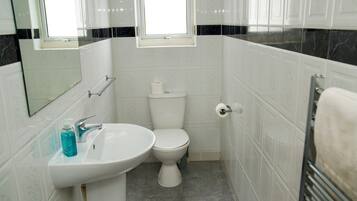 A bathroom with a white sink, toilet, and a window above the toilet.