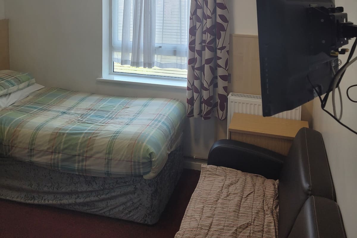 A small room with a bed, a desk, a chair, a window with curtains, and a ceiling light.