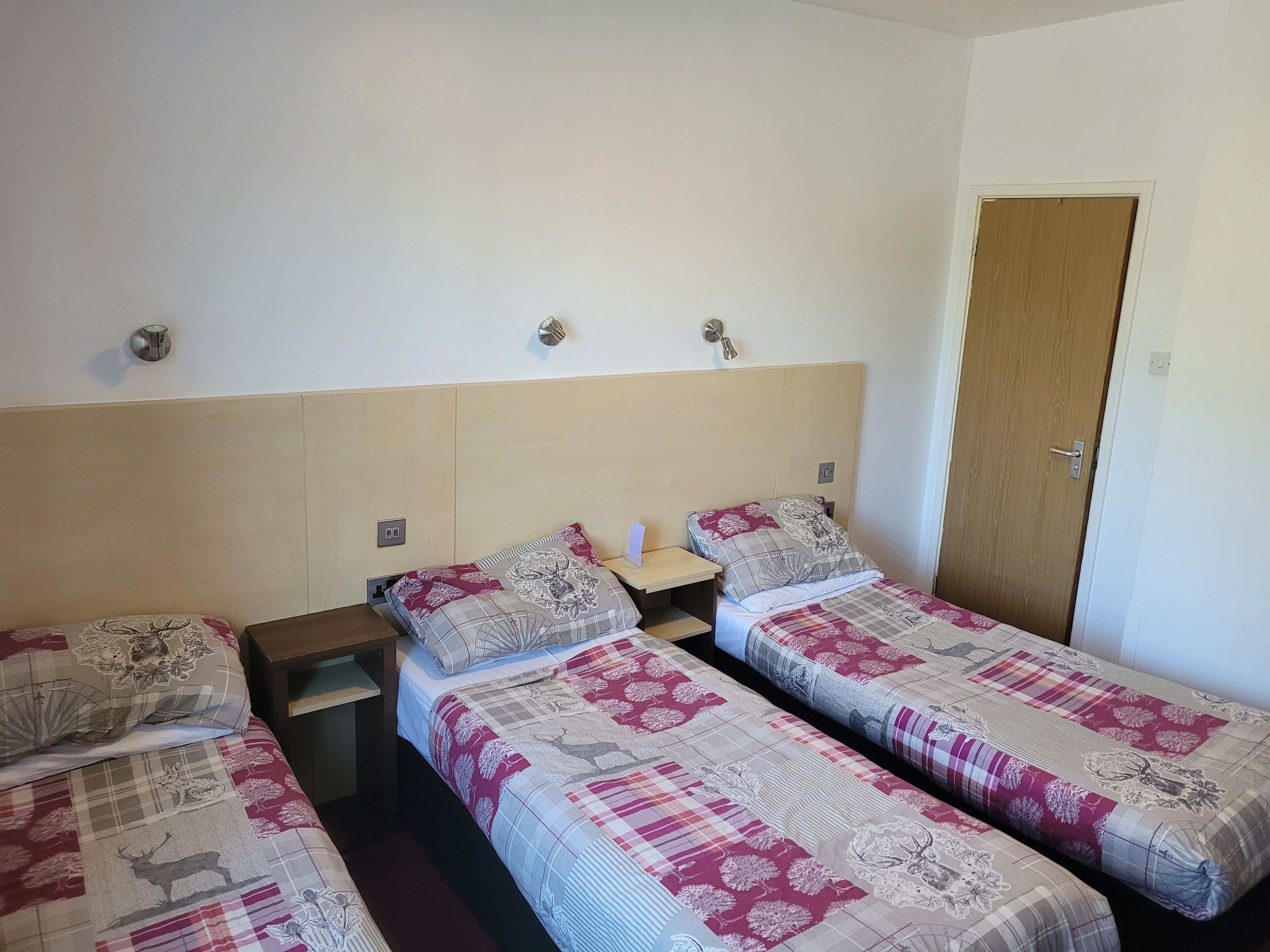 Una habitación con dos camas individuales, cada una con una colcha estampada, una mesita de noche y una lámpara de pared.
