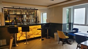 Un espace bar moderne, doté d’un comptoir en marbre, de tabourets et d’une variété de bouteilles et de verres.