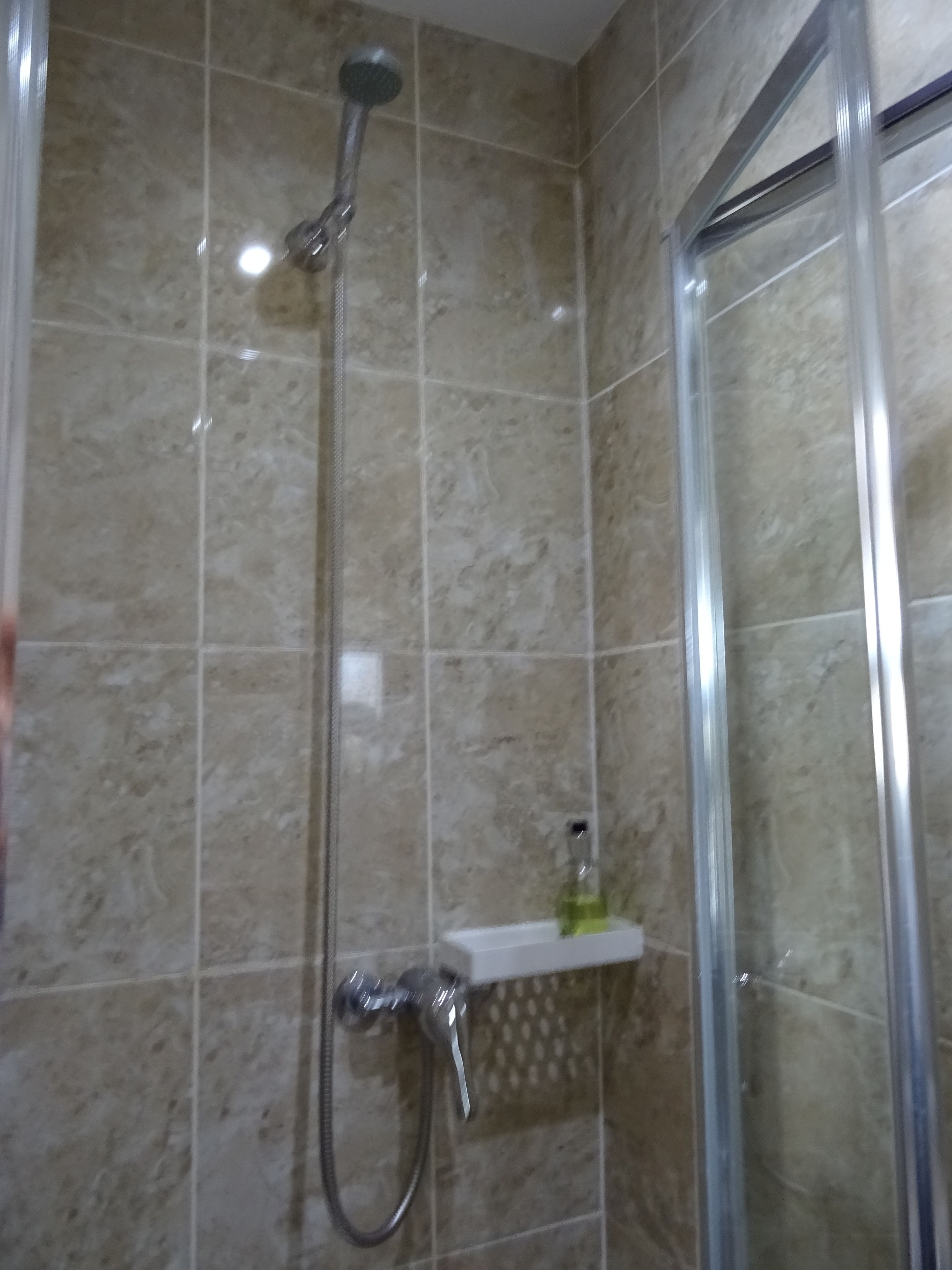 A shower area with a handheld showerhead and a wall-mounted faucet.