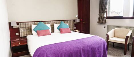 A hotel room with a large bed, a chair, a nightstand, a wardrobe, and a window with curtains.