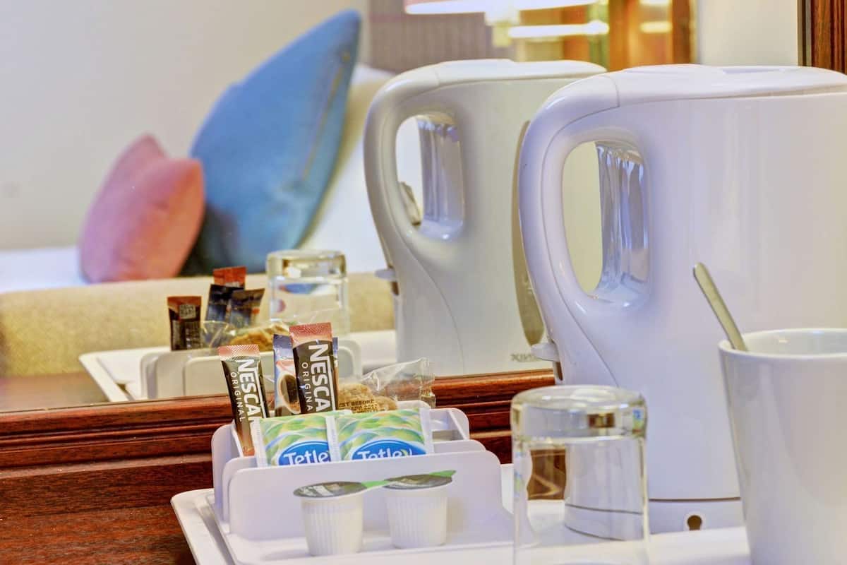 Habitación de hotel con cafetera, una bandeja con cápsulas de café, un vaso de agua y una taza con cuchara.