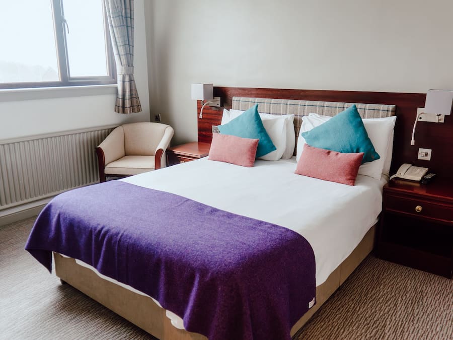 A hotel room with a large bed, a chair, a nightstand with a phone, and a window with curtains.