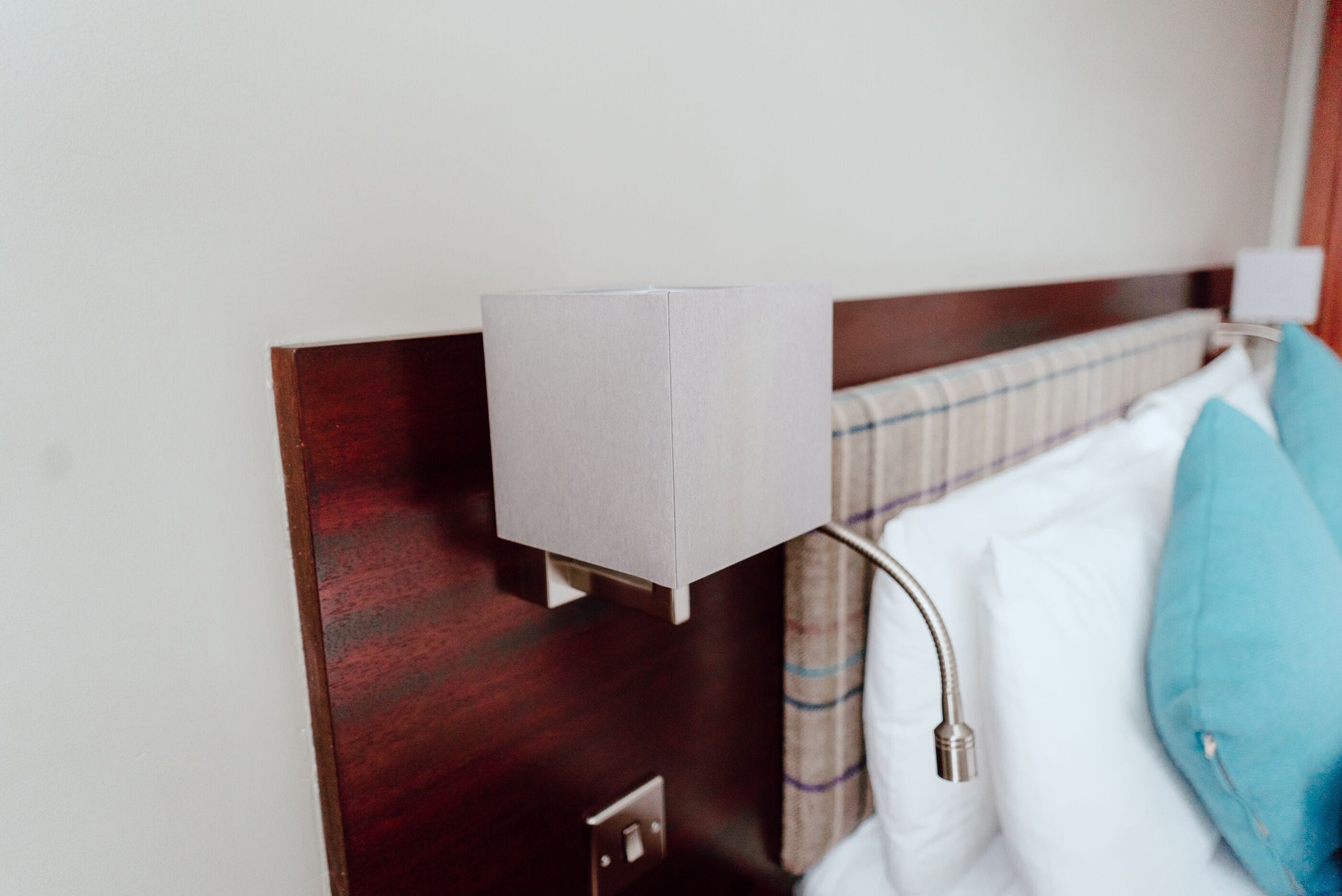 A hotel room with a wooden headboard, a bedside lamp, a white pillow, and a blue jacket hanging on the wall.