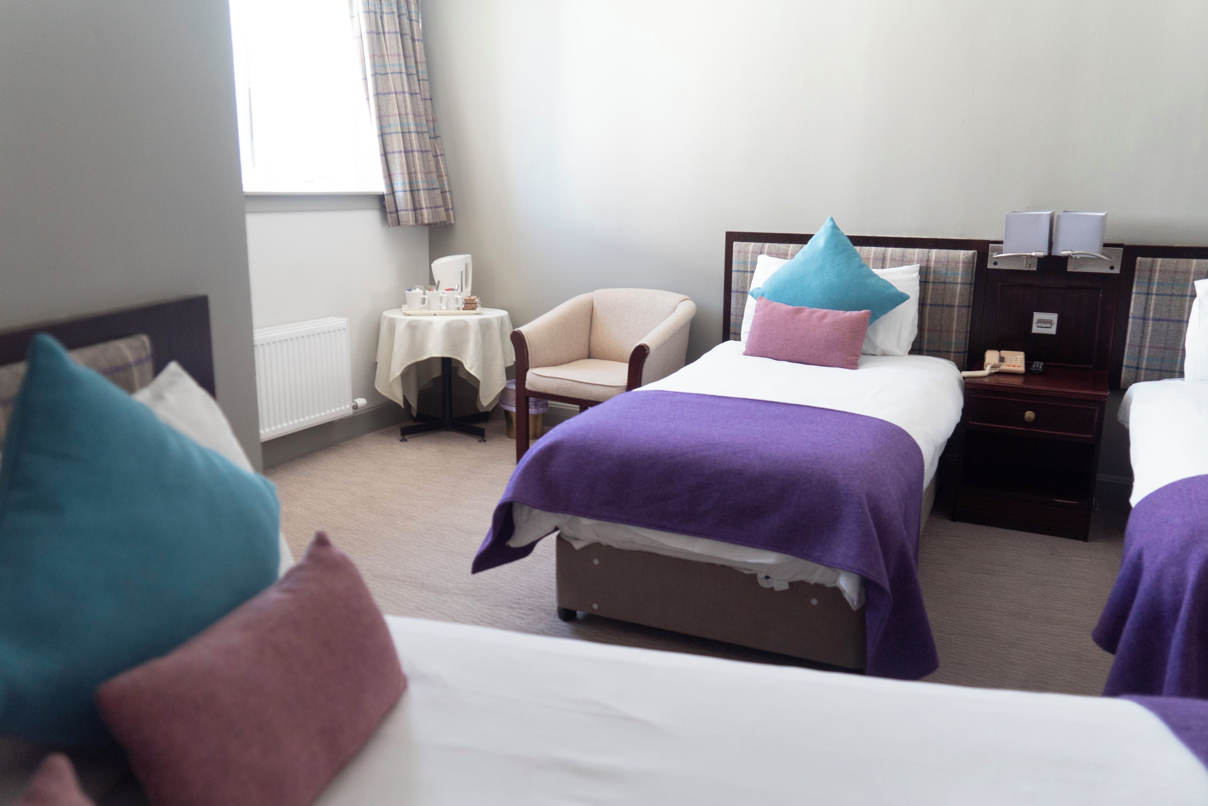 A hotel room with two beds, a chair, a small table, and a nightstand with a lamp.