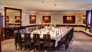 A formal dining room with a long table set for a banquet, flanked by tall chairs, and a bar area with a mirror and decorative lighting. - Caladh Inn (Stornoway)