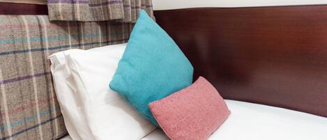 A bed with a white mattress, a teal pillow, and a pink pillow.