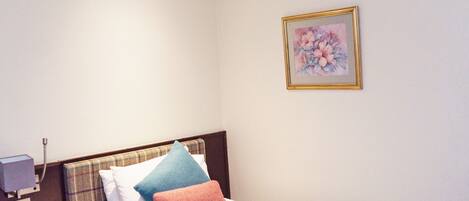 A bedroom with a bed, a nightstand, a bedside table, a wall-mounted picture, and a ceiling light.