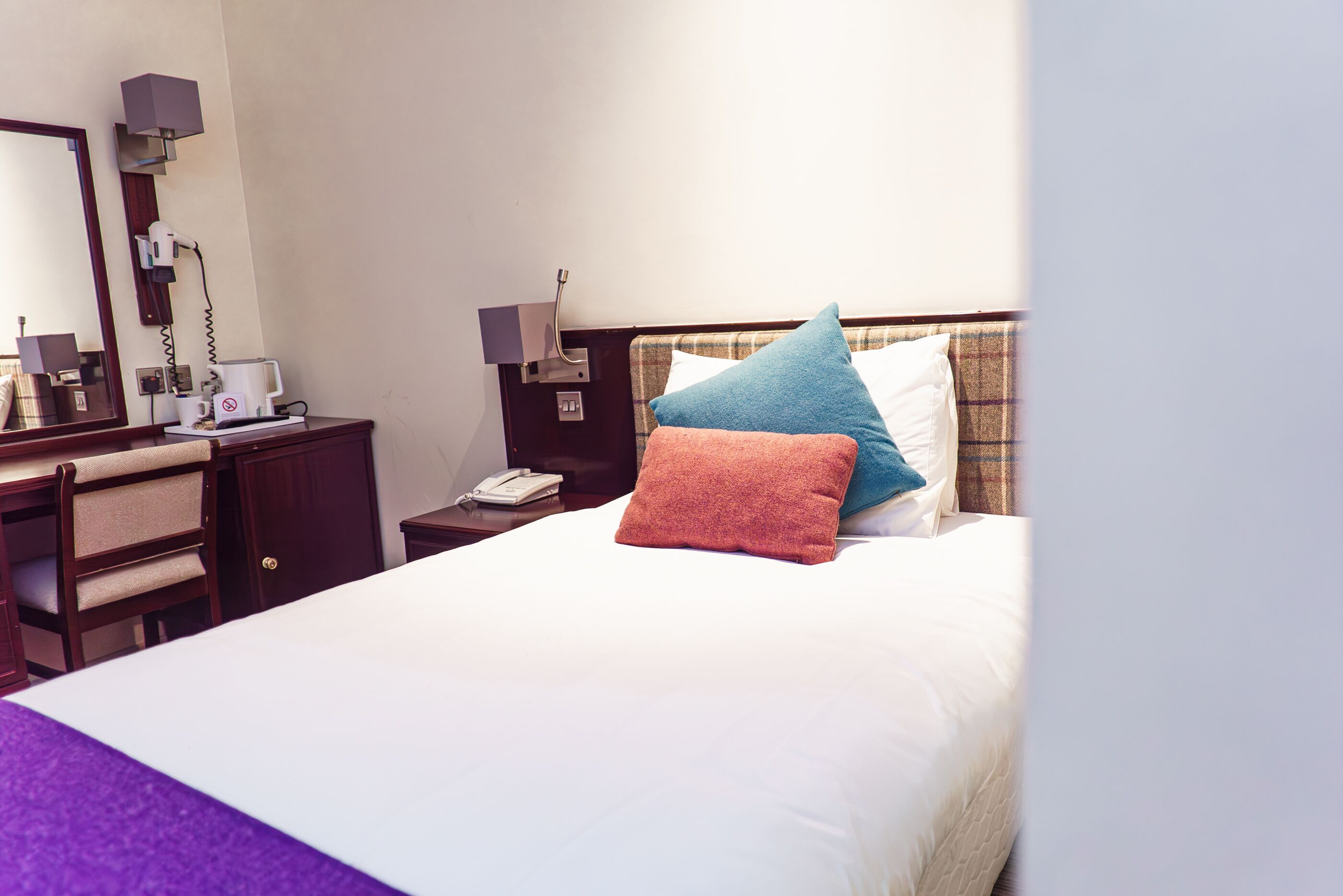 A hotel room with a bed, a bedside table with a lamp, a telephone, and a mirror.