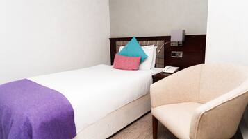 Una habitación de hotel con una cama, una silla, una mesita de noche y una lámpara de pared.