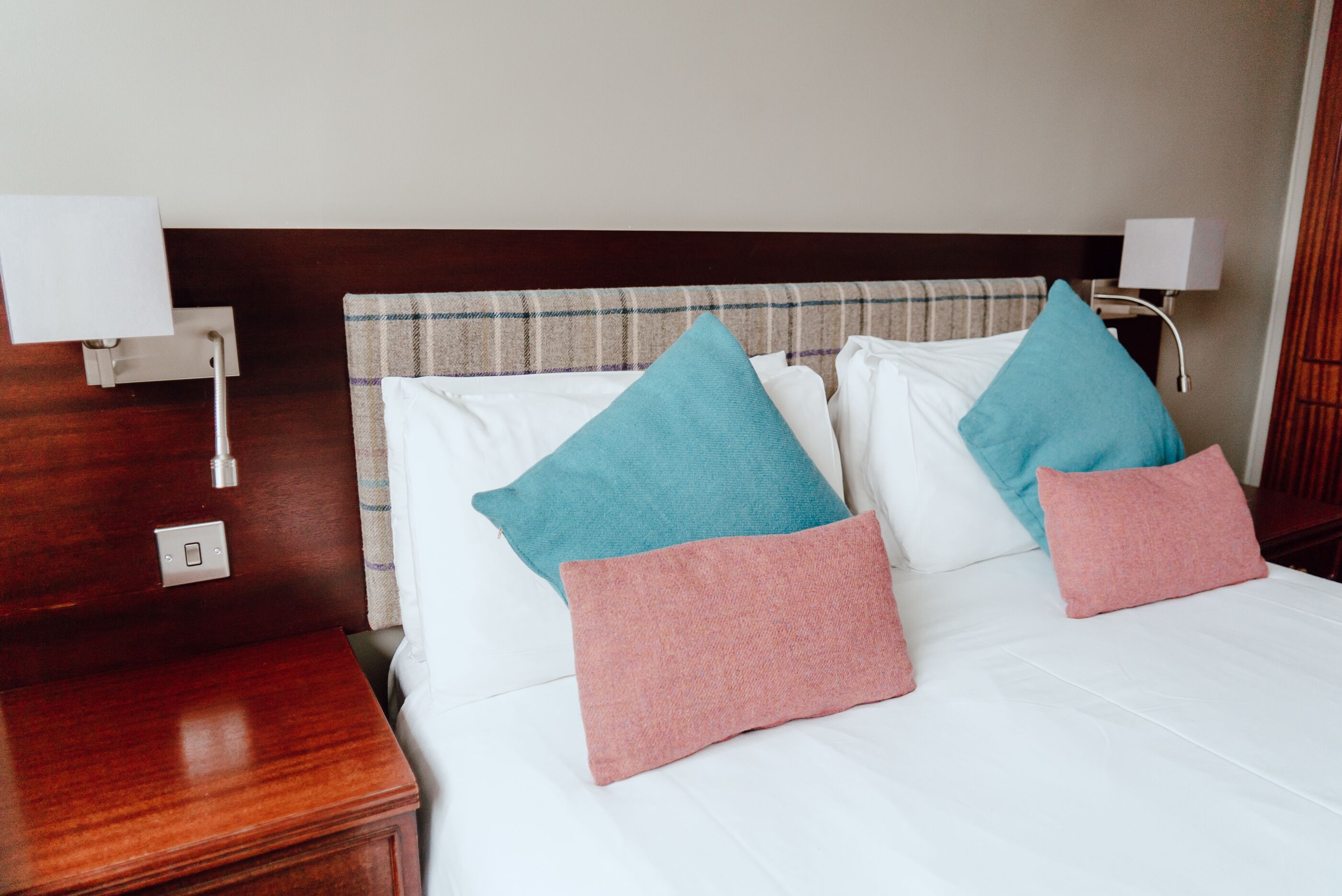 Un lit bien fait, avec des draps blancs et trois oreillers de couleurs différentes.