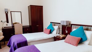 A hotel room with two beds, a wardrobe, a desk with a chair, and a bedside table with a lamp.