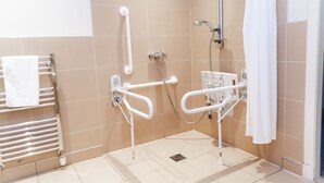A bathroom with beige tiles, a white towel rack, a shower with a white curtain, and a grab bar.
