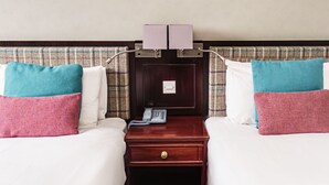 A hotel room with two beds, a nightstand with a telephone, and a wall-mounted light fixture.