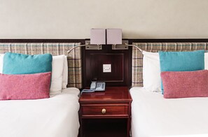 A hotel room with two beds, a nightstand with a telephone, and a wall-mounted light fixture.