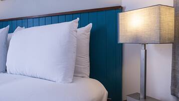 Un lit bien fait, avec du linge de lit blanc et des oreillers, une tête de lit bleue et une lampe de chevet moderne posée sur une table de nuit en bois.