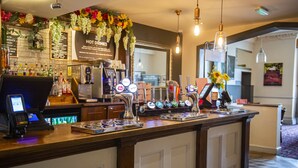 Una zona de bar con barra, grifos de cerveza, una máquina de café y un tablero de menú.