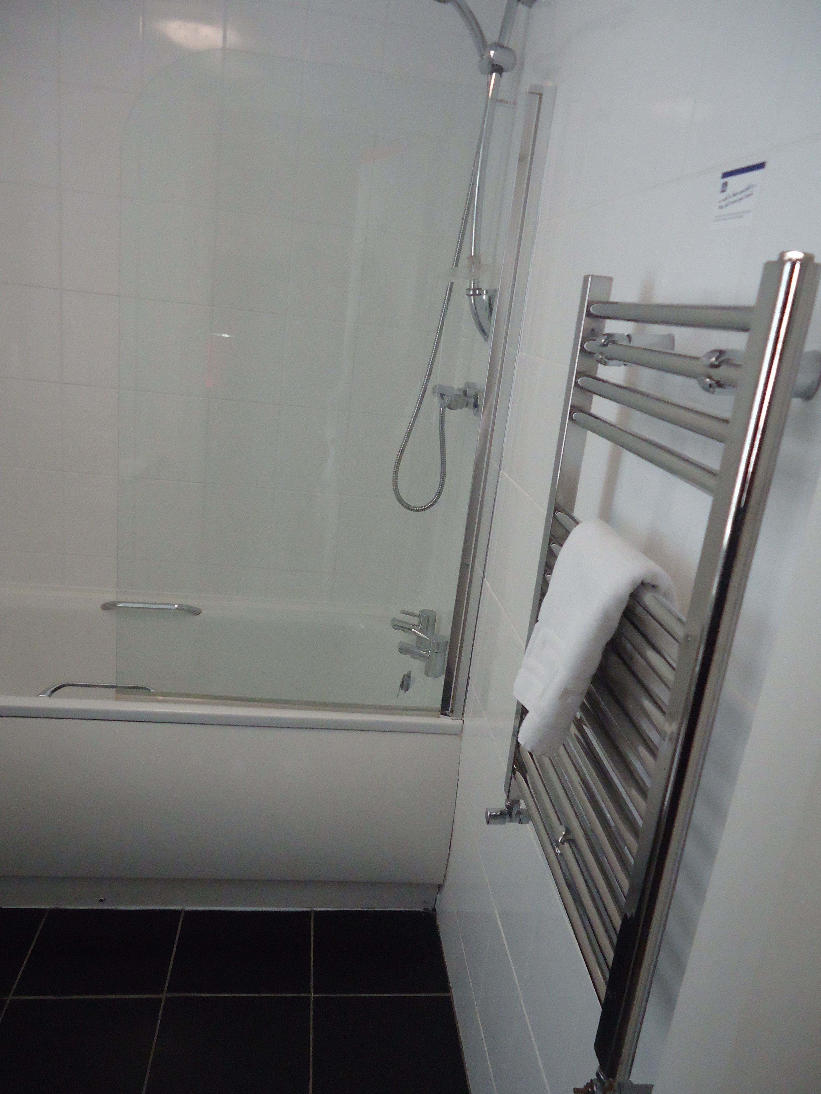 Un bagno con doccia vetrata, una vasca da bagno bianca e un portasciugamani con un asciugamano piegato.