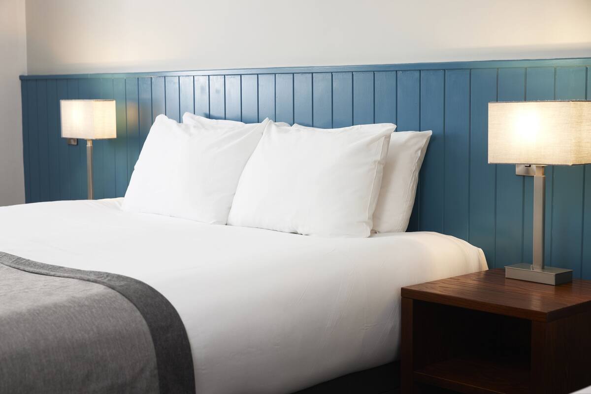 A neatly made bed with white linens, a blue headboard, and two bedside lamps on wooden nightstands.