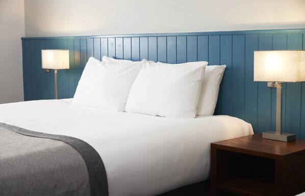 A neatly made bed with white linens, a blue headboard, and two bedside lamps on wooden nightstands.