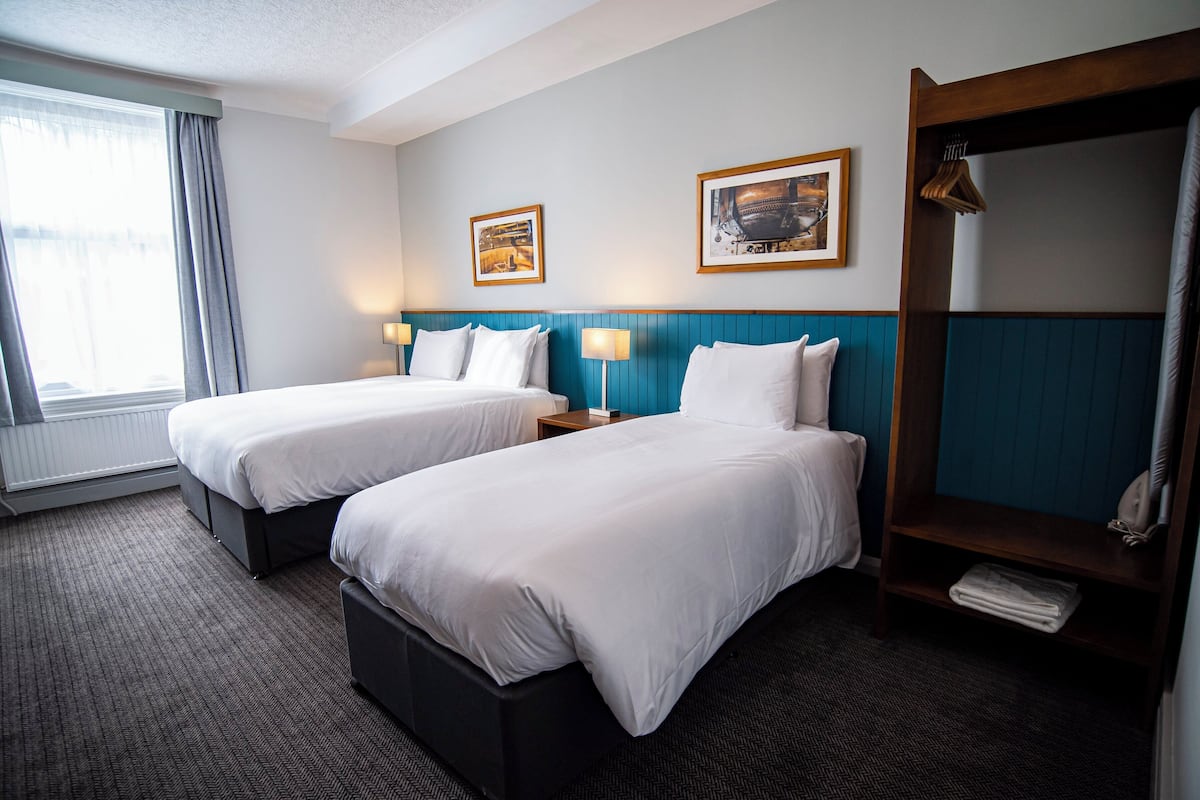 A hotel room with two beds, a large mirror, and two framed pictures on the wall.