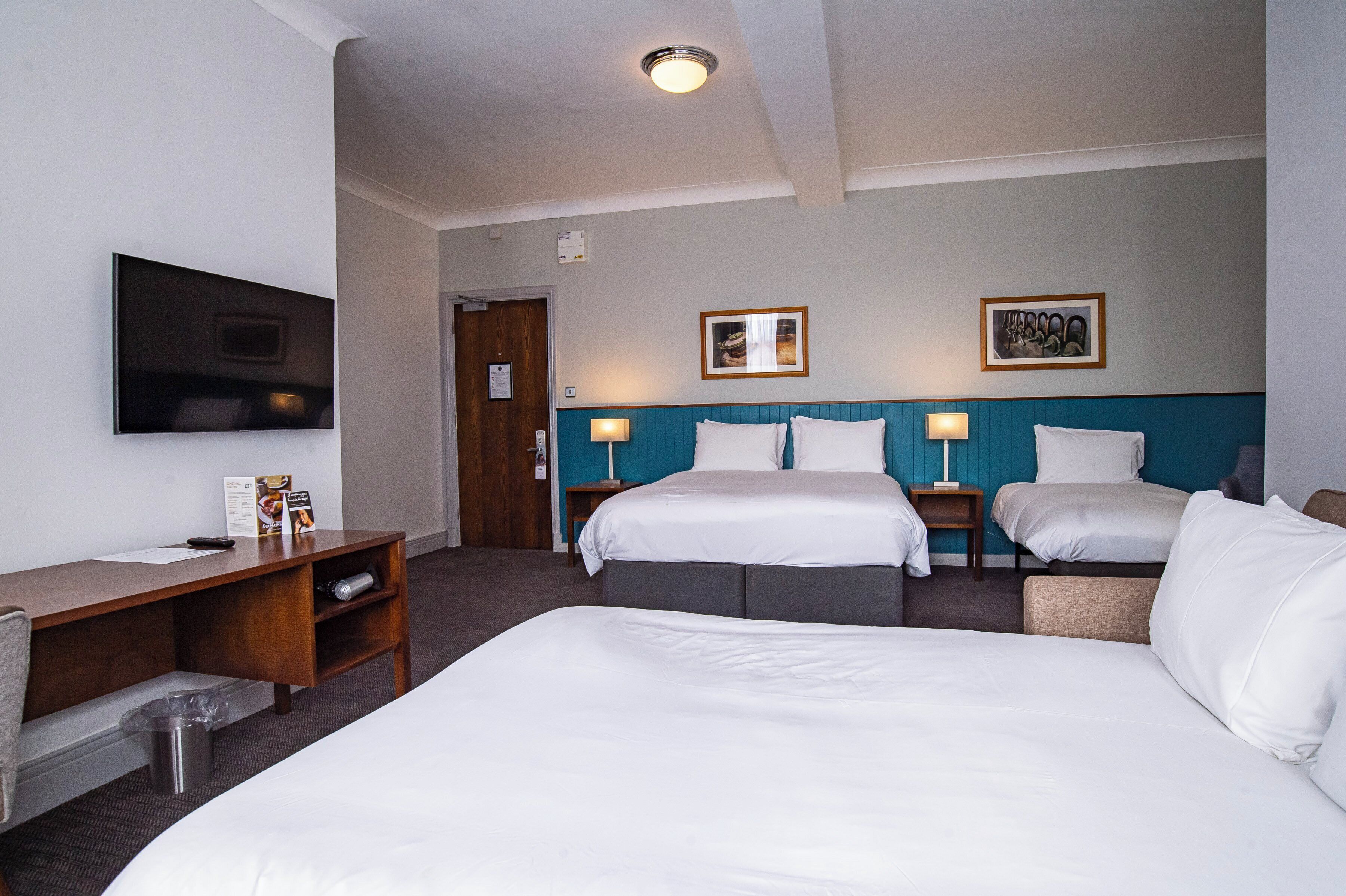 A hotel room with two beds, a desk, a TV, and a trash bin.