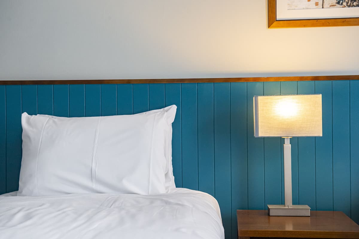 A bed with white bedding, a blue headboard, and a bedside table with a lamp.