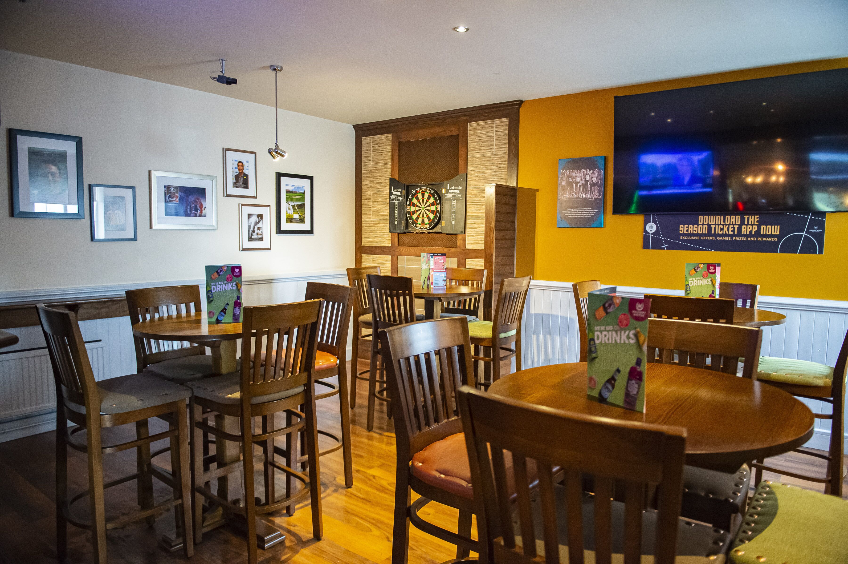 Un restaurante con mesas y sillas de madera, cuadros en la pared y un dardo.