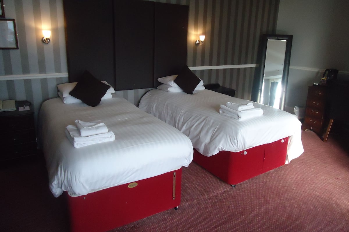 A hotel room with two beds, each with white linens and red bases, a large dark headboard, and a mirror on the wall.