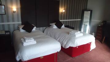 Une chambre d’hôtel avec deux lits, chacun doté de draps blancs et d’un couvre-lit rouge, d’une grande tête de lit sombre et d’un miroir au mur.