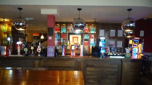 Una zona de bar con mostradores de madera, luces de discoteca colgantes y una variedad de botellas y copas.
