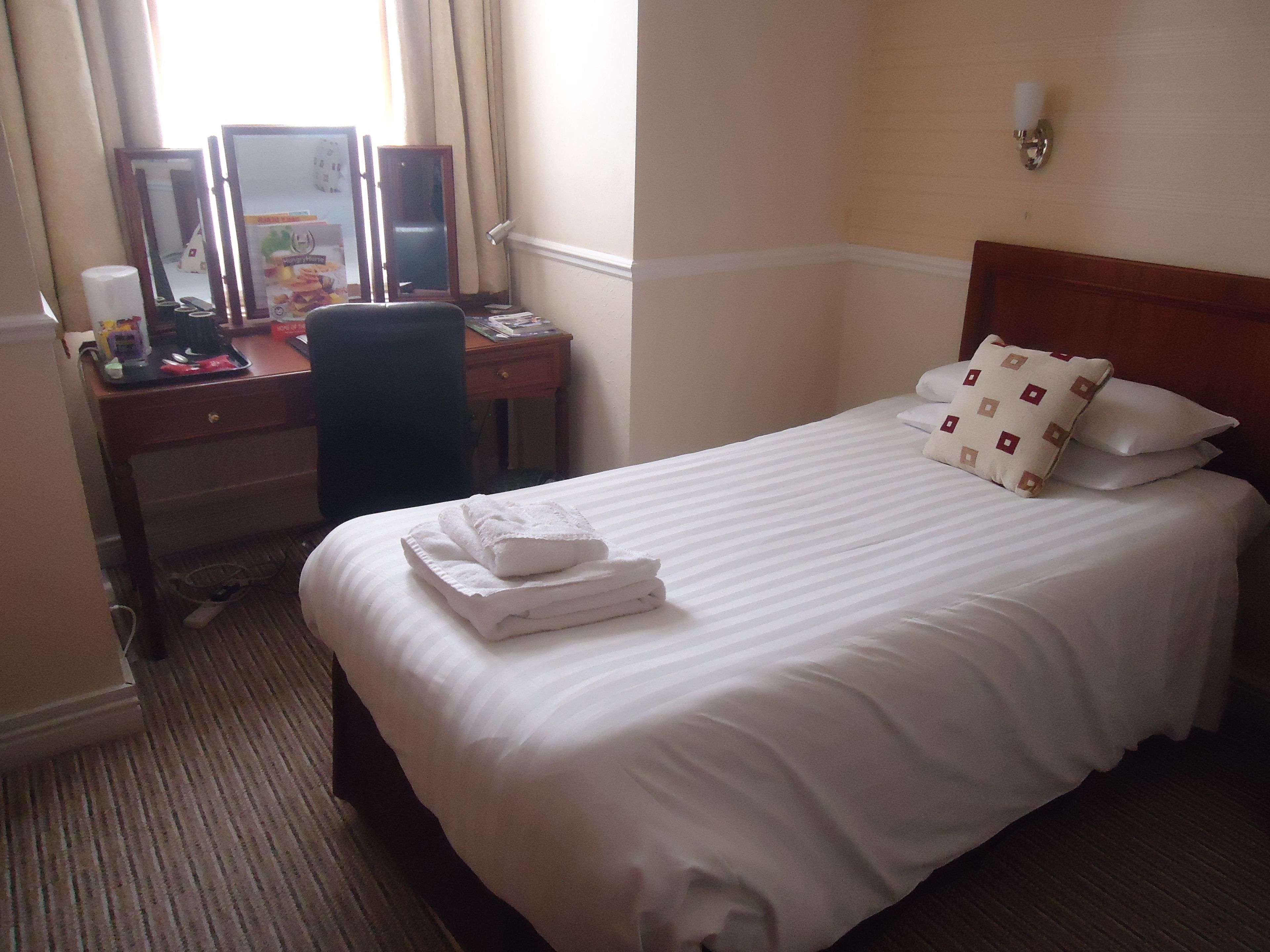 A hotel room with a neatly made bed, a desk with a computer, and a chair.