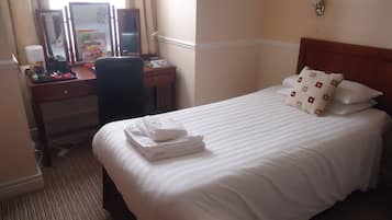 A hotel room with a neatly made bed, a desk with a computer, and a chair.