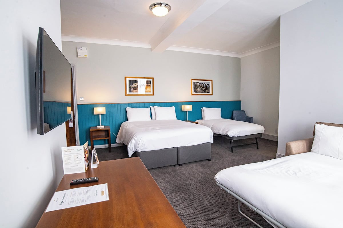 A hotel room with a bed, two bedside tables, a desk, and a TV.