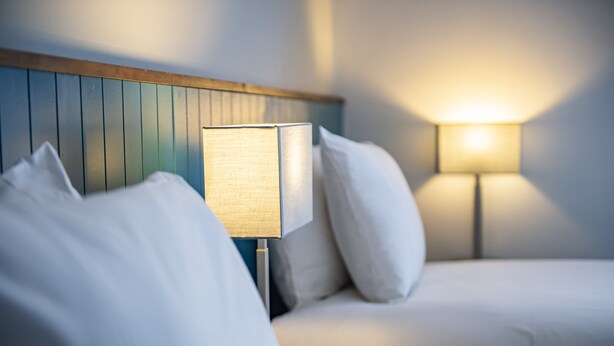 Habitación de hotel con cama, mesita de noche y lámpara de pared.