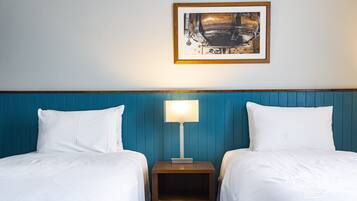 Una habitación de hotel con dos camas, una mesita de noche con lámpara y un cuadro en la pared.