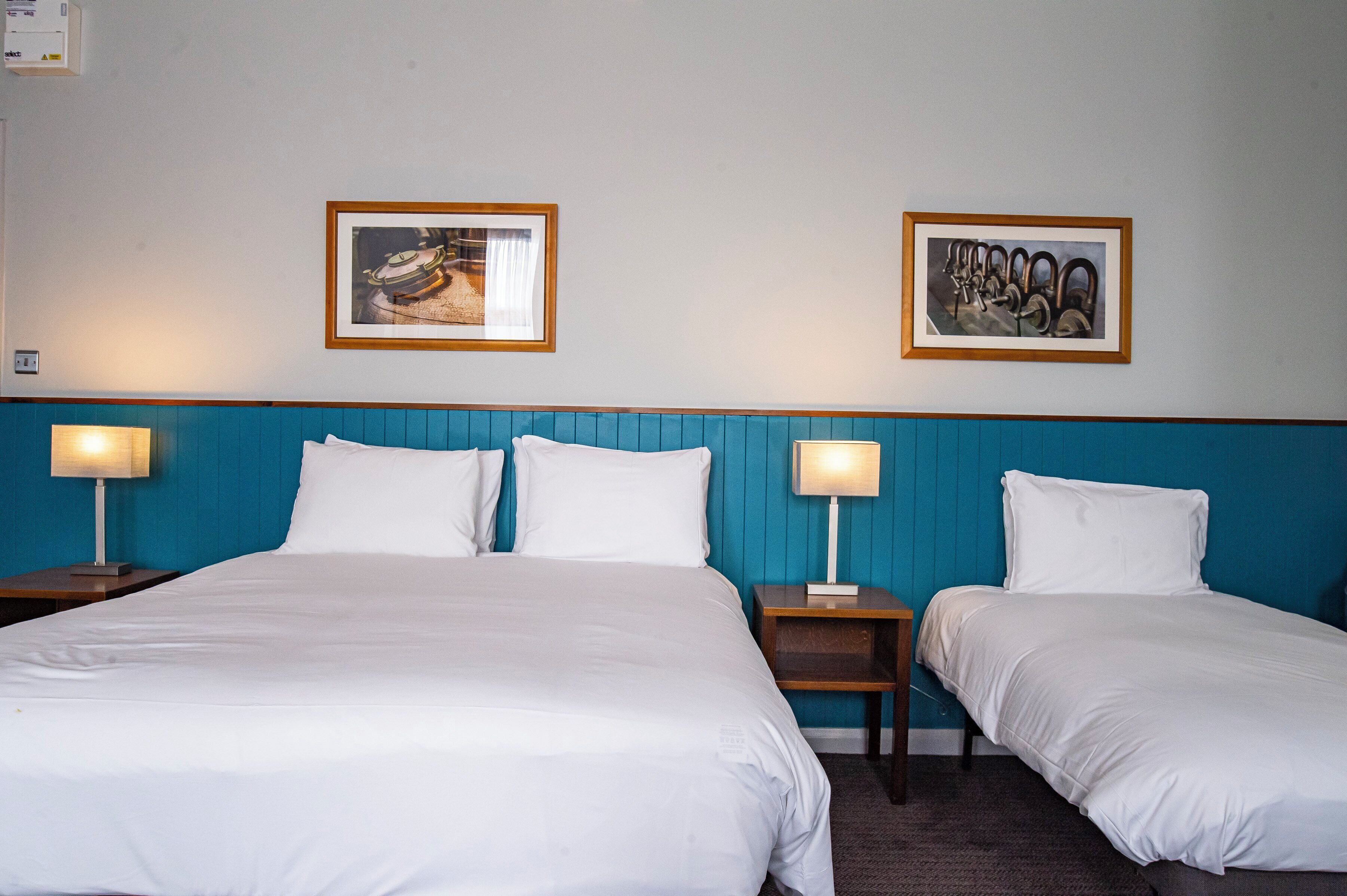 Ein Hotelzimmer mit zwei Betten, einem blauen Kopfteil und zwei gerahmten Bildern an der Wand.