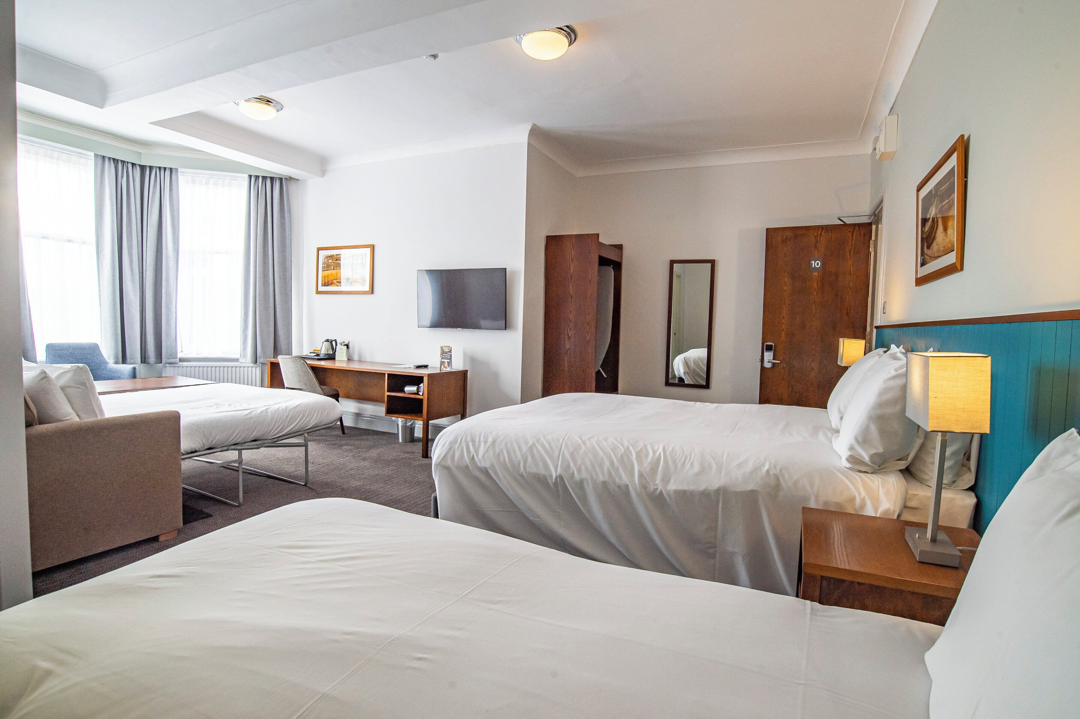 A hotel room with two beds, a desk, a chair, a TV, and a bathroom door.