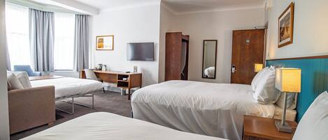 A hotel room with two beds, a desk, a chair, a TV, and a bathroom door.