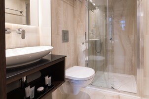 A modern bathroom with a large white sink, a toilet, and a glass-enclosed shower area.