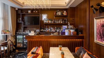 A bar area with a wooden counter, shelves of bottles, a television, and seating with cushions.
