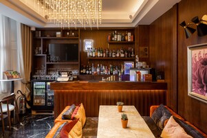 A bar area with a wooden counter, shelves of bottles, a television, and seating with cushions.