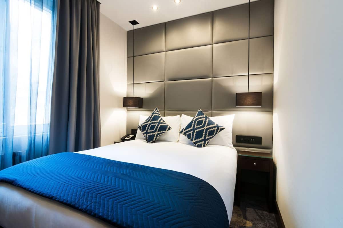 Una habitación de hotel con una cama grande, dos mesitas de noche, un cabecero y una mesita auxiliar.