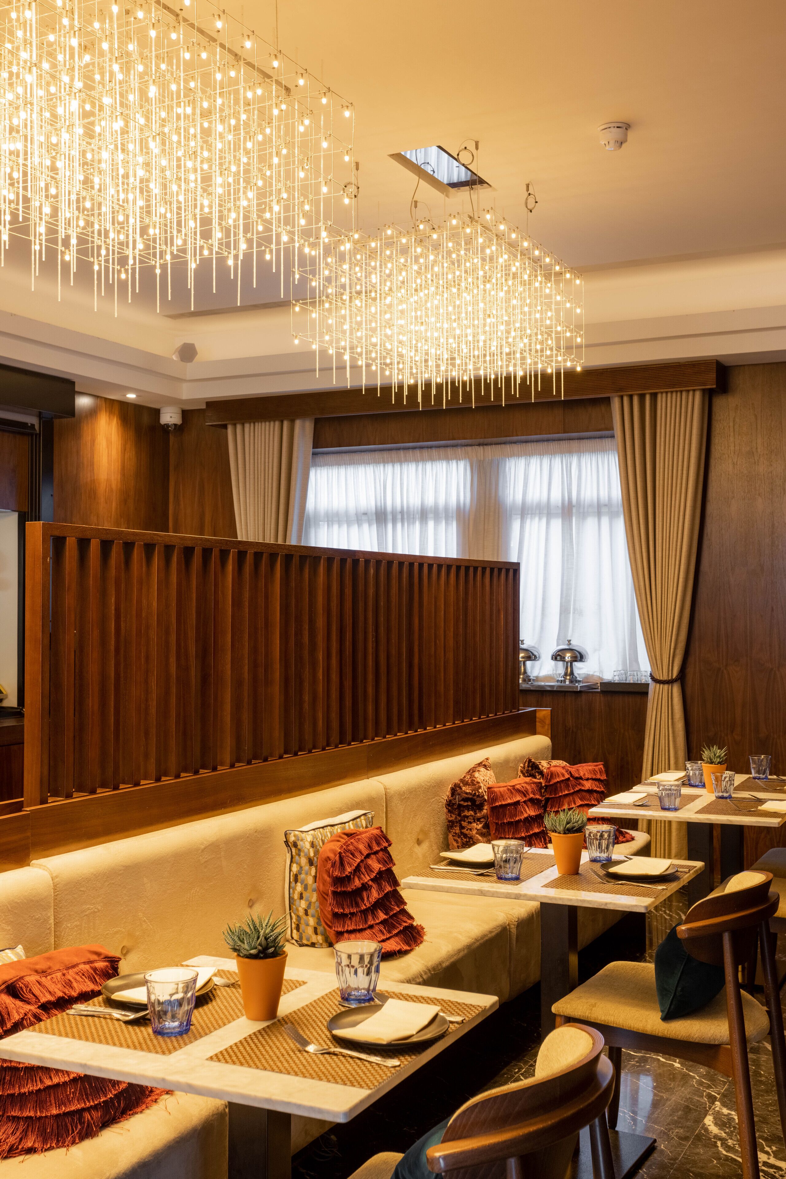 Un restaurante con una larga zona de asientos con bancos de madera, mesas con vajilla y un moderno candelabro.