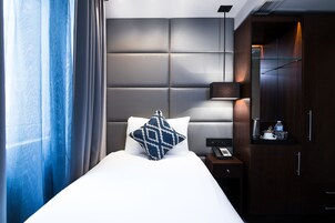 Ein modernes Hotelzimmer mit einem großen Bett, einem Kopfteil mit geometrischem Muster, einem Nachttisch mit Lampe und einem Kleiderschrank.