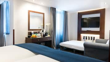 Een hotelkamer met een groot bed, een bureau met spiegel, een flatscreen-televisie en een klein tafeltje met fruit en een plant.