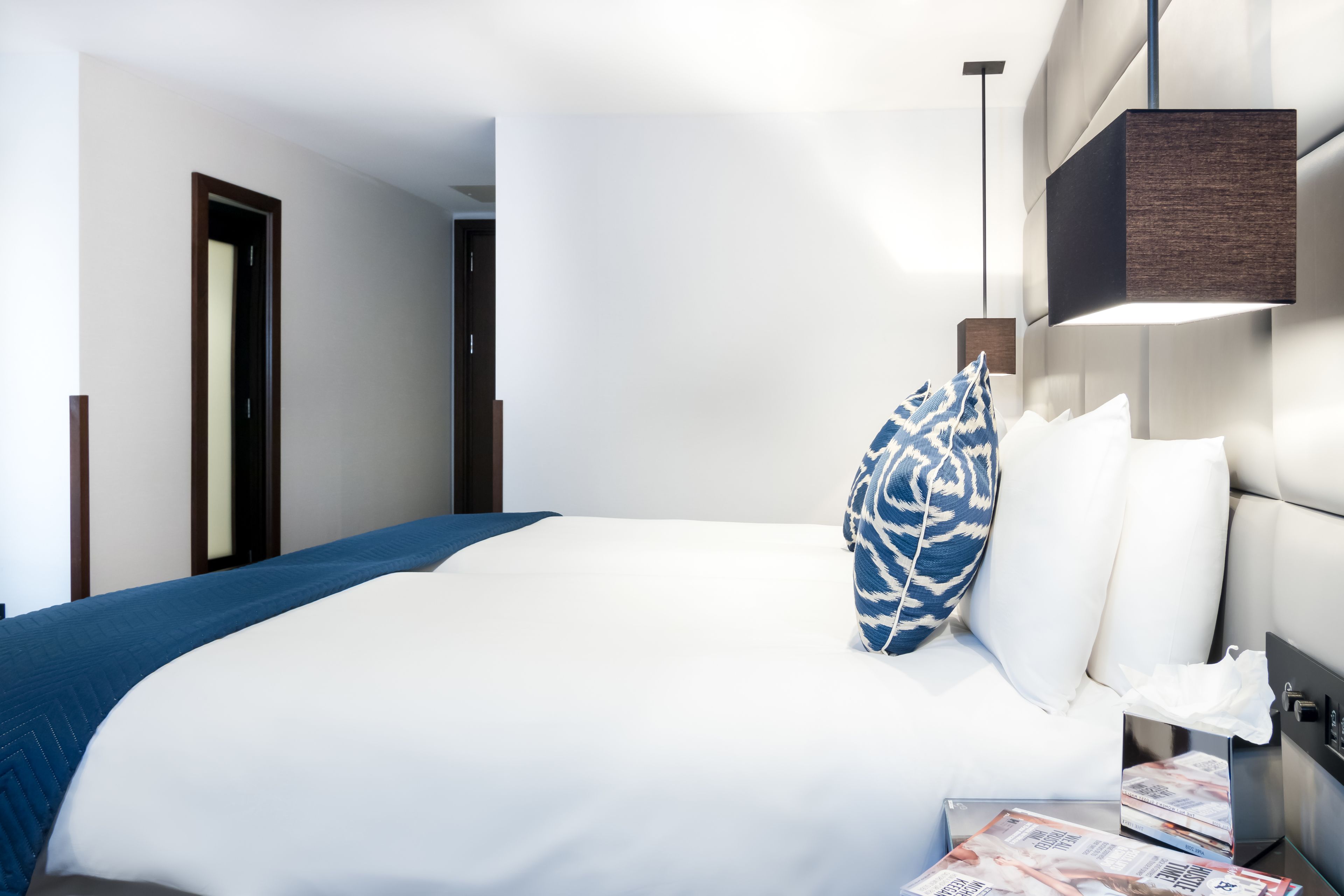 A hotel room with a large bed, a bedside table with a lamp, and a door leading to another room.
